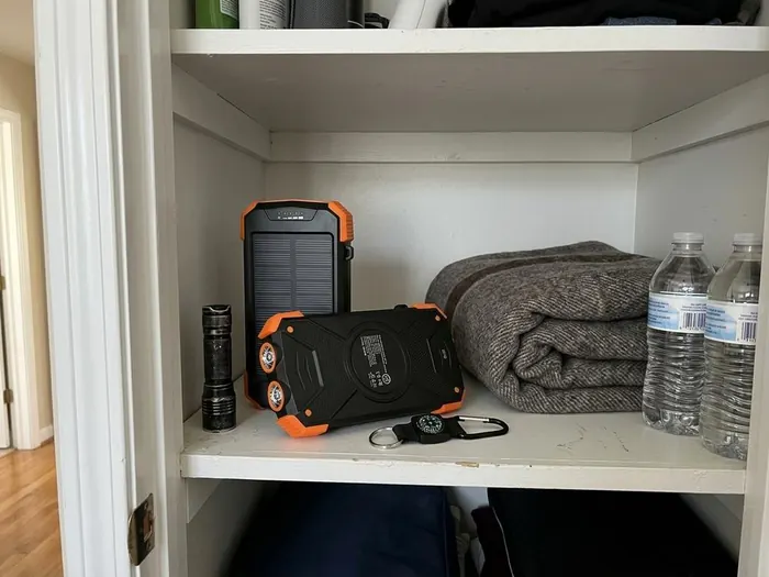 The sealed seed vault pouch on a pantry shelf beside canned goods, bottled water and a folded blanket.